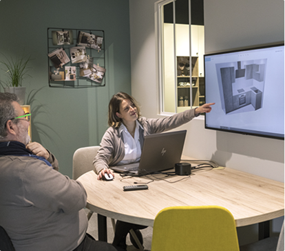 Deux personnes discutent devant un écran affichant un plan de cuisine, assises autour d'une table ronde avec un ordinateur portable.