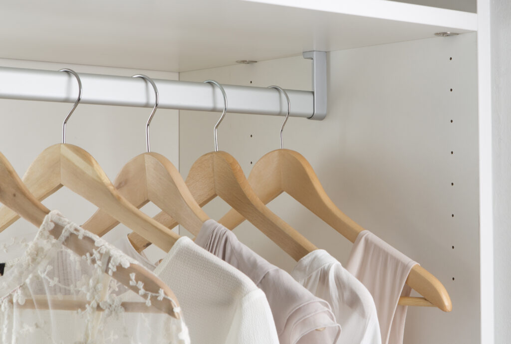 Des cintres en bois suspendent des vêtements blancs et beiges dans une penderie blanche.